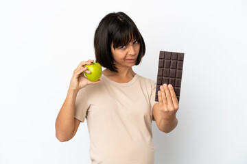 Young mixed race pregnant woman isolated on white background taking a chocolate tablet in one hand...