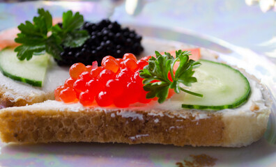 Sandwich with red and black caviar, butter, parsley and cucumber. Birthday and holiday tables.
