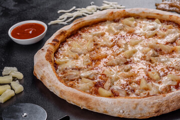 Fresh delicious Italian pizza with chicken, tomatoes and pineapple on a dark concrete background