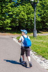 A schoolboy boy is traveling on a scooter.