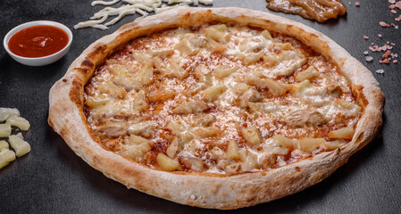 Fresh delicious Italian pizza with chicken, tomatoes and pineapple on a dark concrete background