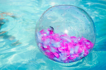 Inflatable beach ball transparent with pink feathers inside floating on the surface of the open sea pool