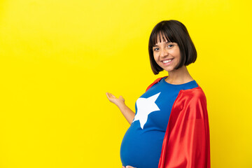 Super Hero pregnant woman isolated on yellow background extending hands to the side for inviting to come