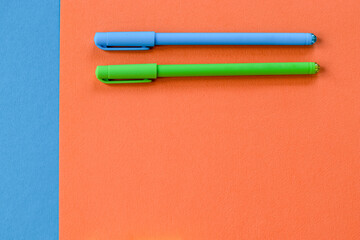 Minimum set of school and office supplies on bright orange and blue background. Two pens banner. Concept: back to school. Flatlay, top view.