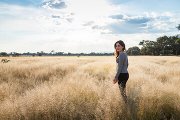 Naklejka na ściany i meble Young adult smiling Mexican woman standing in a dry grassy meadow looking back at the camera