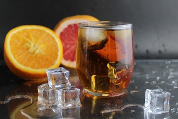 Apple citrus dark juice in a glass next to lies citrus orange grapefruit ice on a black background. Refreshing drinks, summer, soft drinks