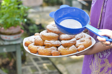 woman's hand sprinkles sugar topping on a donuts with blurred background