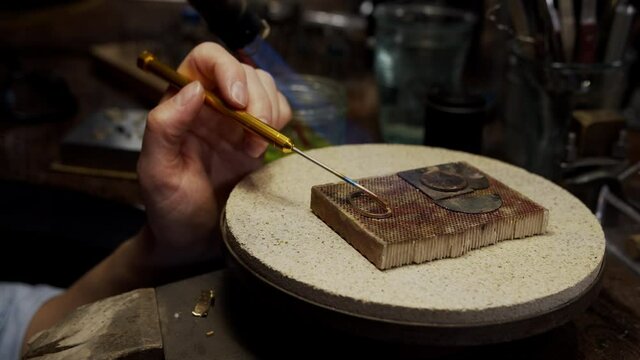Jeweller applying gold and forming an engagement ring in her workshop.