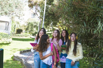 Group of latinx teenage girlfriends going to school with their books and backpacks smiling