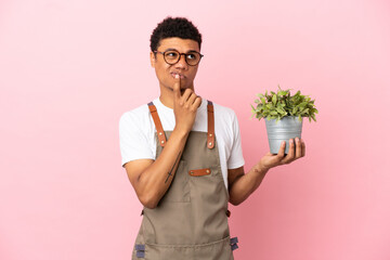 Gardener African man holding a plant isolated on pink background having doubts while looking up