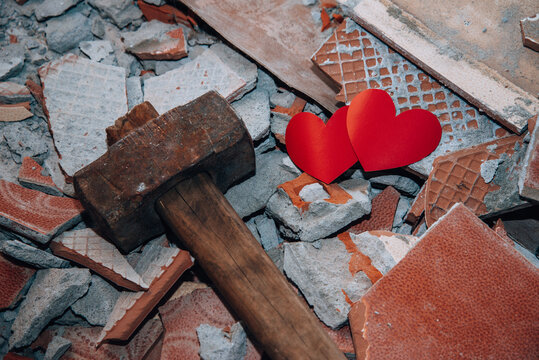 Two hearts among shards next to hammer. Concept of broken love. Unhappy relationships. Difficult period in family life. Quarrel. Endured scandal. Love against all odds. Infidelity and betrayal