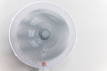 a white fan blows against the background of a white wall. A fan with a grid is located at home in...