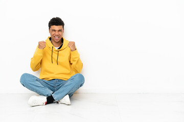 Young African American man sitting on the floor isolated on white background celebrating a victory in winner position