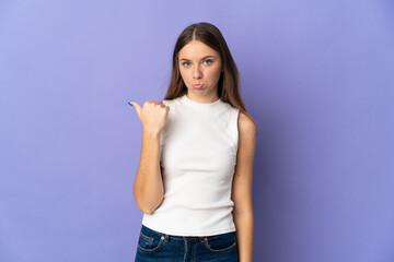 Young Lithuanian woman isolated on purple background unhappy and pointing to the side