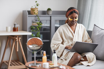 Portrait of young African-American woman using laptop while enjoying skincare routine at home and relaxing, copy space