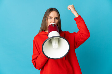 Young Lithuanian woman isolated on blue background shouting through a megaphone to announce...
