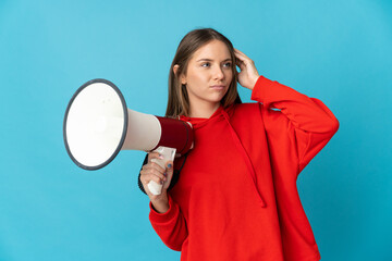 Young Lithuanian woman isolated on blue background holding a megaphone and having doubts