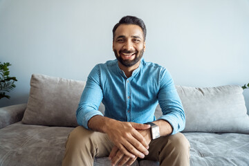Portrait of indian man toothy smiling to camera sitting on sofa webcam view