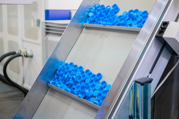 Production line: many blue plastic bottle caps moving on conveyor belt of automatic compression...