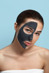 Portrait of a beautiful woman  with a black mask of clay on her face ..Girl model beauty face with cosmetic mask . Skin care . Spa treatment. Cosmetology