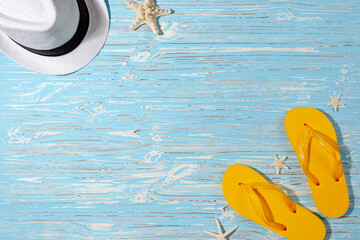 yellow rubber flip flops, white beach hat, starfish on a blue wooden background