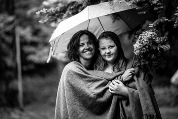 A woman and her teenage daughter together in the park under an umbrella. Black and white photo.