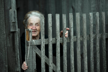 An old woman in the village street near the wooden fence.