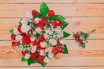 Wedding bouquet of white and red roses with green leaves on a wooden floor background