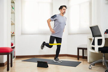 Middle aged man with beard doing exercise at home looking at video on tablet