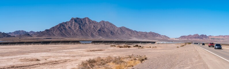 Panoramic View of Highway With Large Solar Farm on the Side of the Road and Large Mountains...