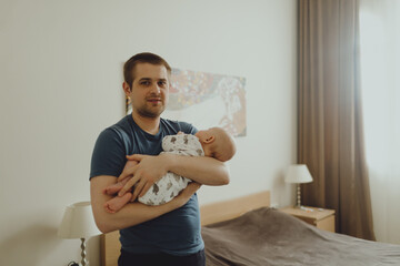 father carries a sleeping baby in his arms around the apartment