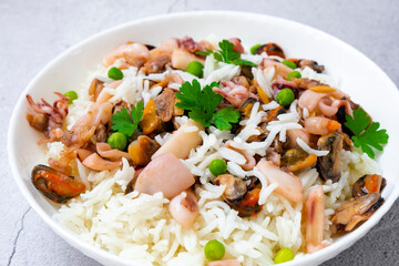 Close-up plate with seafood risotto, rice with mussels, baby octopus, squid, shrimps and parsley stewed in white wine. Traditional Italian seafood paella. Healthy Mediterranean cuisine recipe.
