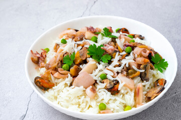 Seafood risotto in white plate, rice with mussels, baby octopus, squid, shrimps and herbs stewed in white wine. Traditional French seafood paella. Tasty Mediterranean cuisine recipe.