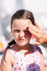 the father's hand applies sunscreen from burns and ultraviolet light on the daughter's face on a hot sunny day on the beach. 
