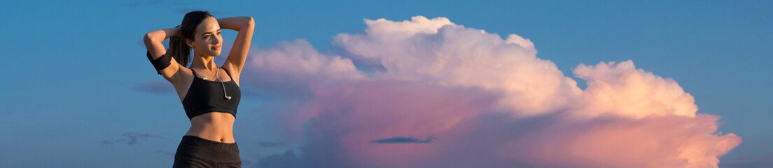 A sporty slim girl in leggings and a top is standing near a concrete wall with a training mat, resting between exercises.