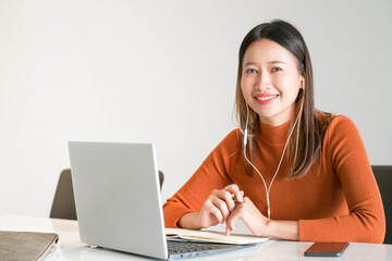 Beautiful Asian business woman freelance use laptop computer with internet for online working or virtual seminar with writing on note book at home. Female study and learn online course on video call