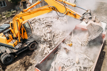 Excavator loads construction waste into truck for removal from construction site. Demolition of...