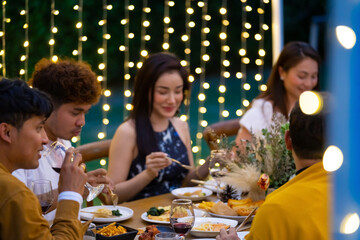 Group of diversity Asian millennial people friends enjoy outdoor garden dinner party eating food and drinking wine with talking together. Reunion friendship meeting celebration and night life concept.