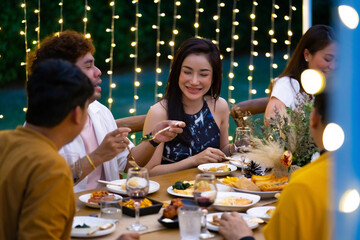 Group of diversity Asian millennial people friends enjoy outdoor garden dinner party eating food and drinking wine with talking together. Reunion friendship meeting celebration and night life concept.