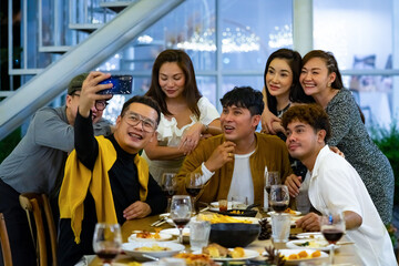 Group of Happy diversity Asian millennial people friends enjoy outdoor dinner party and using smartphone taking selfie together. Reunion friendship meeting celebration party and night life concept.