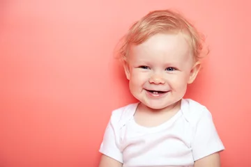 Fototapeten portrait caucasian curly blond smiling baby girl with two teethon pink background wearing in white t-shirt. copy space. © yana136