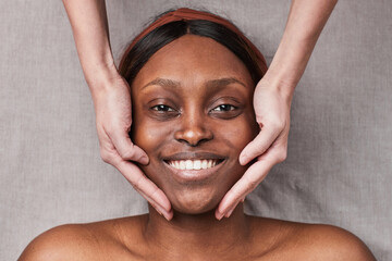 Top down view at smiling African-American woman enjoying face massage and looking at camera
