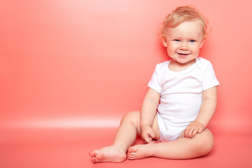 portrait caucasian curly blond smiling baby girl sitting on pink background wearing in white t-shirt. copy space.