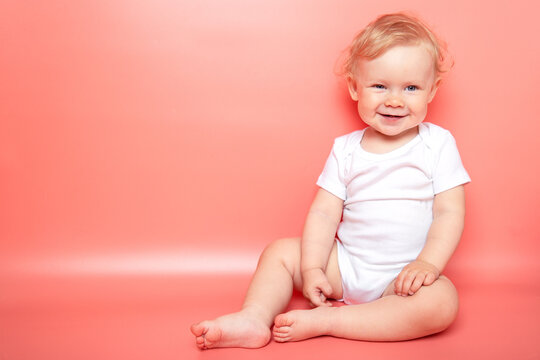 Portrait Caucasian Curly Blond Smiling Baby Girl Sitting On Pink Background Wearing In White T-shirt. Copy Space.