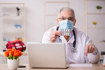 Old male doctor working in the clinic during pandemic