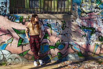 young woman posing on a wall with murals and drawings.