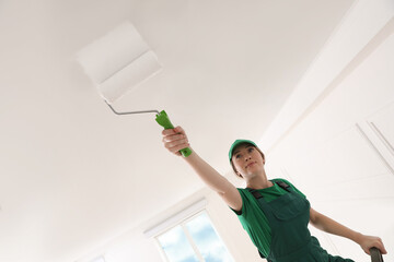 Worker painting ceiling with white dye indoors