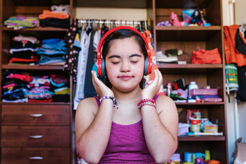 portrait of latin girl teenager with Down syndrome listen to music with headphones in home in...