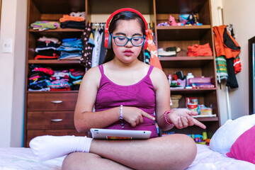 portrait of mexican female teenager with Down syndrome listen to music with headphones in home in disability concept in Latin America	
