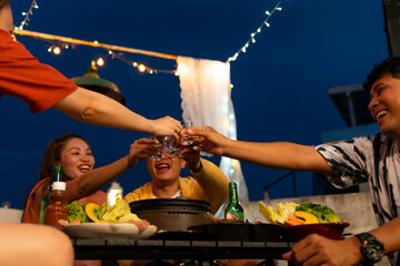 Group of Asian millennial people friends toasting alcoholic drink shot glasses while having outdoor dinner party with eat barbecue grill at rooftop for meeting reunion and holiday celebration together - obrazy, fototapety, plakaty